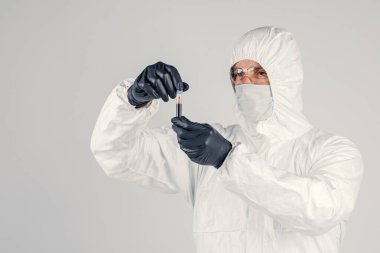 Bir adamın elinde test tüpü yakın plan, elinde kırmızı sıvı tutan tıbbi maskeli bir adam. Kan örnekleri, tıbbi ve kimyasal araştırmalar.