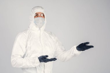 Tek kullanımlık anti-bakteriyel izolasyon giysisi içindeki bir insan epidemiyoloğu beyaz arka planda el hareketlerini gösteriyor. Salgın ve tıbbi konsept.