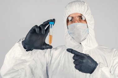 Bir adamın elinde test tüpü yakın plan, elinde kırmızı sıvı tutan tıbbi maskeli bir adam. Kan örnekleri, tıbbi ve kimyasal araştırmalar.