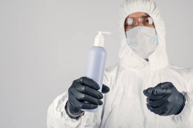Tıbbi koruyucu maskeli bir adam, el dezenfektanı tutuyor.