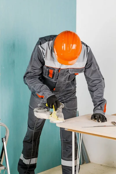 A young man, a carpenter polishes a wooden Board with an orbital sander. The concept of construction and repair. — Stock Image Young Man Carpenter Polishes Wooden Board Orbital Sander Concept Construction Stock Photo