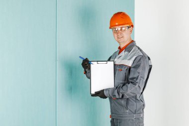 Bir erkek mühendis, koruyucu kasklı ve gözlüklü bir inşaat işçisi bir tablete yazıyor. Yenileme ve inşaat konsepti