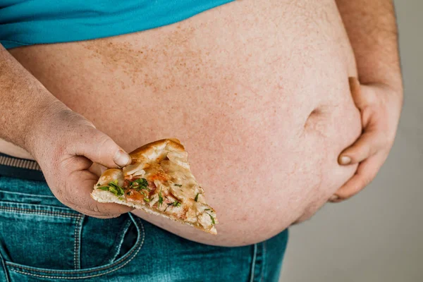 Fat man with a slice of pizza on a gray background, the concept of unhealthy food.