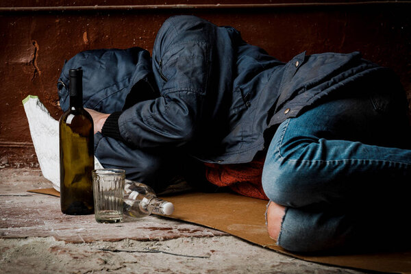 A homeless man, a drunk, fell asleep on the street. The concept of alcoholism and homelessness.