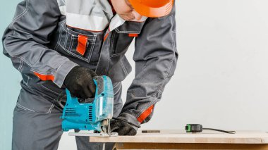 Erkek bir inşaatçı elektrikli bir yap-boz ile tahta bir kirişi keser, erkek eli elektrikli bir yap-boz ile. Bir ağaçla çalışmak