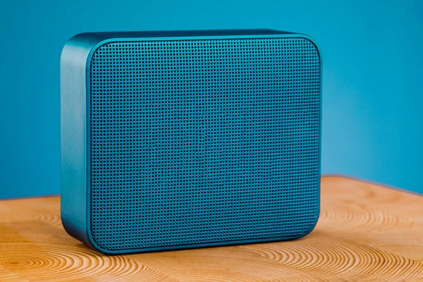 Portable blue wireless speaker, on a wooden table on a blue background