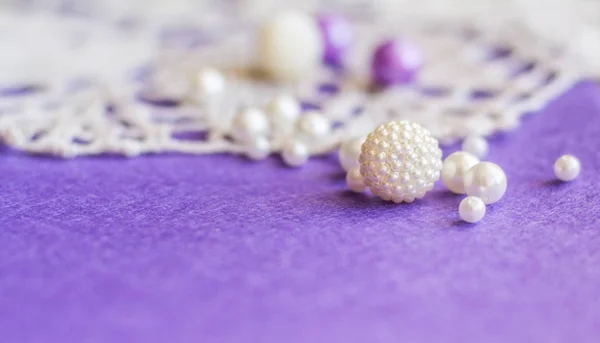 Sewing accessories background. Pearl beads and lace on a background of lilac felt. Selective focus.