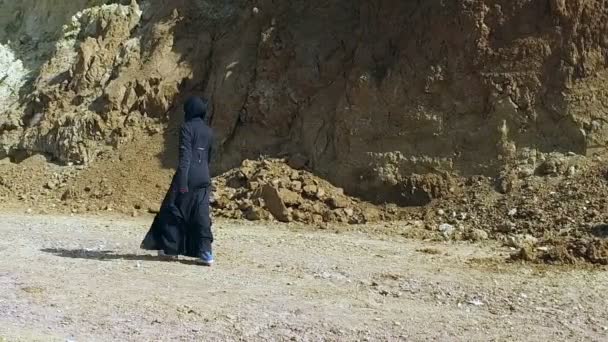 Ein Mädchen in einem schwarzen Abay geht an steinigen Hügeln entlang. — Stockvideo
