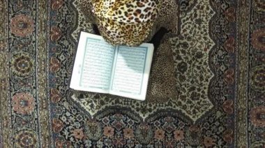 O halının üzerinde oturan Kur'an okur.