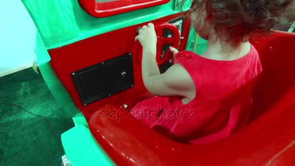 Маленька дівчинка в червоній сукні повертає кермо на машині — стокове відео