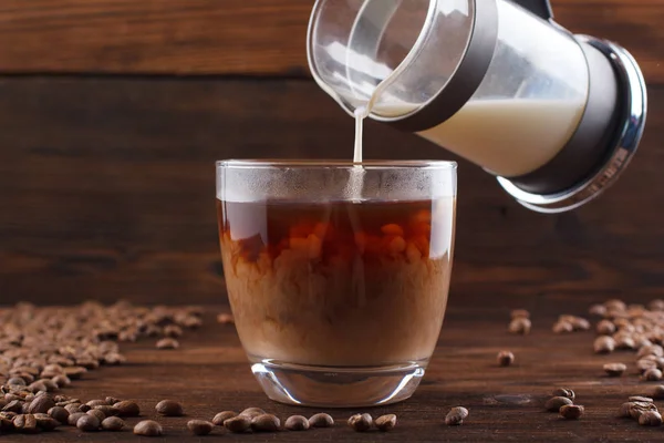 Coffee with milk in a transparent cup. Milk is poured into coffee on a wooden background — Stock Photo, Image