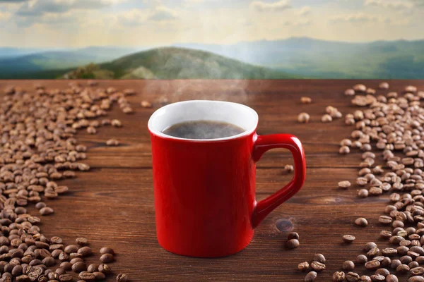 Red cup of hot coffee on a wooden background, on a background of mountains. Smoking coffee, steaming — Stock Photo, Image