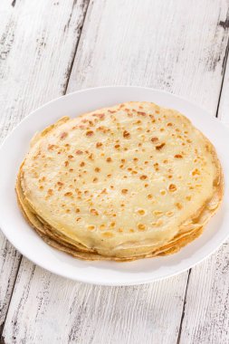 Beyaz bir plaka üzerinde ince krep. Maslenitsa. Hafif ahşap arka plan üzerinde Rus krep. Bir rustik tarzda.