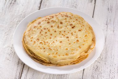 Beyaz bir plaka üzerinde ince krep. Maslenitsa. Hafif ahşap arka plan üzerinde Rus krep. Bir rustik tarzda.