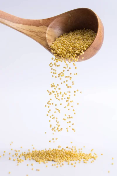Spoon of pours millet falling on a white background — Stock Photo, Image