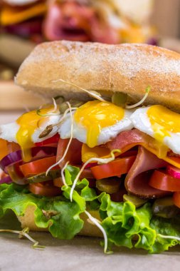 Bir sandviç pastırma, peynir ile kızarmış bıldırcın yumurtası. Taze sebze ve otlar ahşap arka plan üzerinde bir sandviçle.