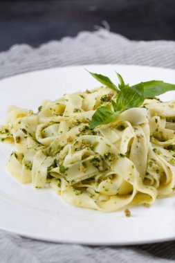 Natürmort - fesleğen ve roka karanlık bir arka plan üzerinde beyaz bir tabak içinde yeşil pesto ile ev yapımı makarna.