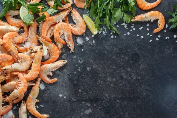 Crevettes avec citron vert, glace, herbes et sel de mer sur fond noir. Cadre pour votre texte. Crevettes aux herbes et épices éparpillées sur fond noir. Contexte alimentaire . — Photo