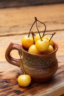 Sarı kiraz ahşap arka plan üzerinde bir rustik tarzda. Meyveleri olgunlaşmış taze kiraz bir fincan.