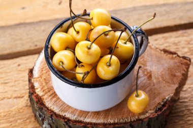 Sarı kiraz ahşap arka plan üzerinde bir rustik tarzda. Meyveleri olgunlaşmış taze kiraz bir fincan.