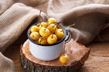 Sarı kiraz ahşap arka plan üzerinde bir rustik tarzda. Meyveleri olgunlaşmış taze kiraz bir fincan.