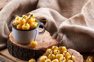 Sarı kiraz ahşap arka plan üzerinde bir rustik tarzda. Meyveleri olgunlaşmış taze kiraz bir fincan.