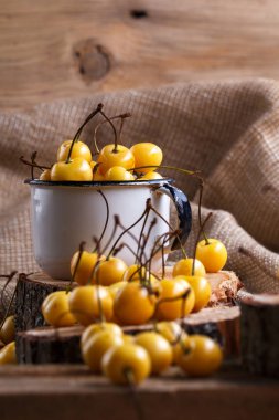 Sarı kiraz ahşap arka plan üzerinde bir rustik tarzda. Meyveleri olgunlaşmış taze kiraz bir fincan.