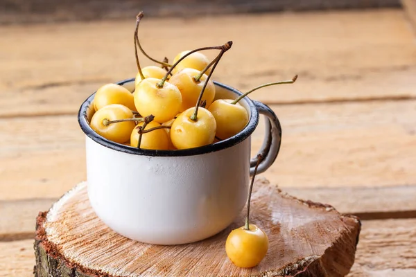 Sarı kiraz ahşap arka plan üzerinde bir rustik tarzda. Meyveleri olgunlaşmış taze kiraz bir fincan.