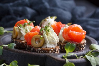 Somon, süzme peynir, zeytin karanlık bir arka plan üzerinde mikro yeşillikleri ile lezzetli kanepe. Soğuk meze.