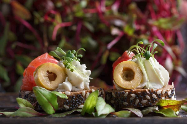 Somon, süzme peynir, zeytin karanlık bir arka plan üzerinde mikro yeşillikleri ile lezzetli kanepe. Soğuk meze.