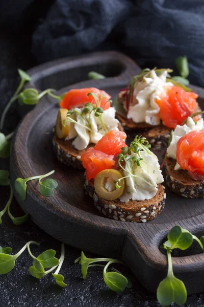 Somon, süzme peynir, zeytin karanlık bir arka plan üzerinde mikro yeşillikleri ile lezzetli kanepe. Soğuk meze.