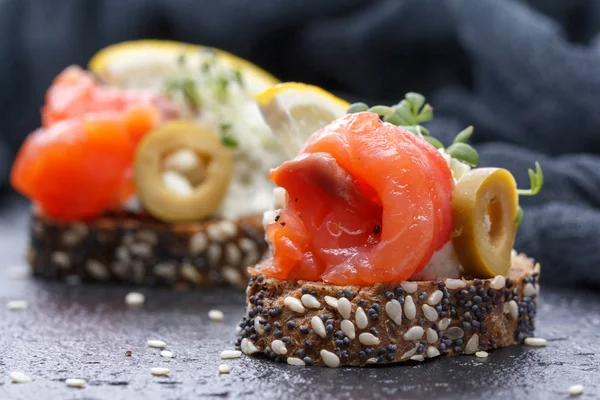 Karanlık bir arka plan üzerine somon ve peynir peynirli kanepe.