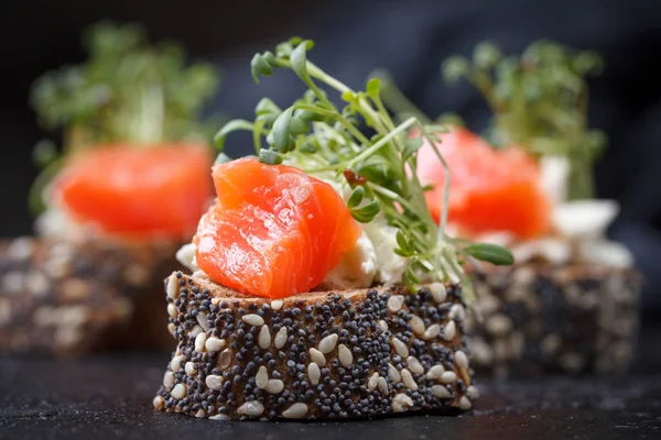 Karanlık bir arka plan üzerine somon ve peynir peynirli kanepe.