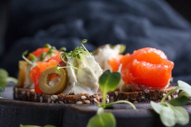 Somon, süzme peynir, zeytin karanlık bir arka plan üzerinde mikro yeşillikleri ile lezzetli kanepe. Soğuk meze.