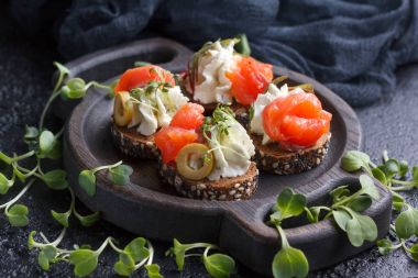 Somon, süzme peynir, zeytin karanlık bir arka plan üzerinde mikro yeşillikleri ile lezzetli kanepe. Soğuk meze.