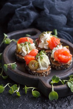 Somon, süzme peynir, zeytin karanlık bir arka plan üzerinde mikro yeşillikleri ile lezzetli kanepe. Soğuk meze.