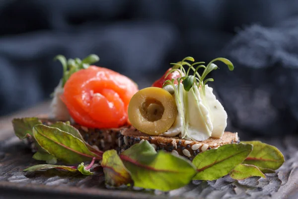 Somon, süzme peynir, zeytin karanlık bir arka plan üzerinde mikro yeşillikleri ile lezzetli kanepe. Soğuk meze.