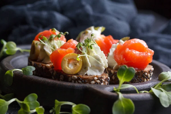 Somon, süzme peynir, zeytin karanlık bir arka plan üzerinde mikro yeşillikleri ile lezzetli kanepe. Soğuk meze.