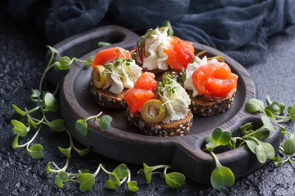 Somon, süzme peynir, zeytin karanlık bir arka plan üzerinde mikro yeşillikleri ile lezzetli kanepe. Soğuk meze.