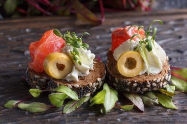 Somon, süzme peynir, zeytin karanlık bir arka plan üzerinde mikro yeşillikleri ile lezzetli kanepe. Soğuk meze.