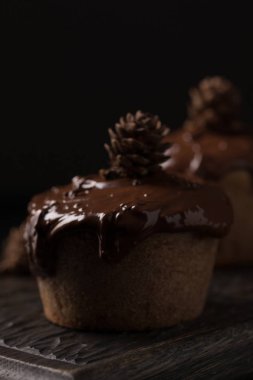 Çikolatalı kek, koyu ahşap arka plan üzerinde küçük bir koni ile dekore edilmiştir. Cupcakes koyu çikolata ve kakao tozu ile dökülür. Olağandışı dekorasyon ile cupcakes. Düşük anahtar