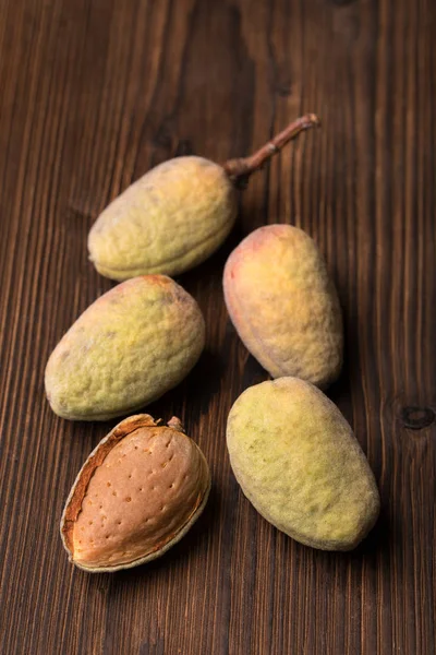Fresh harvest of almonds on a wooden background. Green and brown nuts. Shell and peel of almonds.