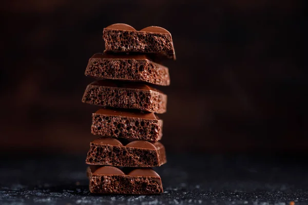Chocolate poroso apilado sobre fondo negro. Pedazos de chocolate poroso con leche, uno encima del otro. Coloque debajo de su texto . — Foto de Stock