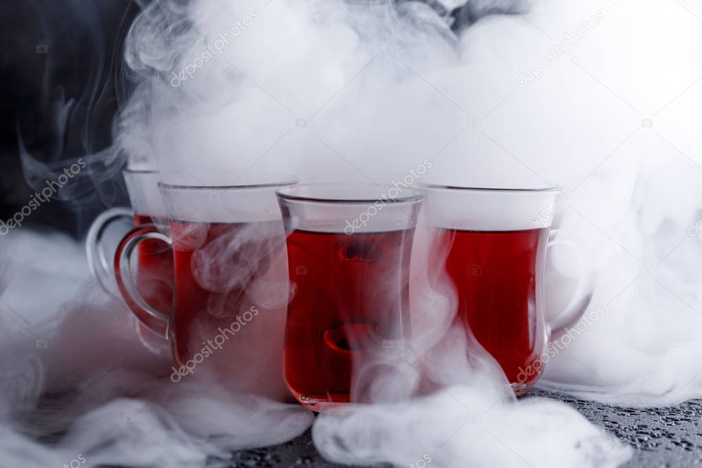 red cocktail with ice vapor. red cold tea with steam on a black background.