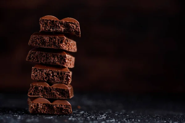 Chocolate poroso apilado sobre fondo negro. Pedazos de chocolate poroso con leche, uno encima del otro. Coloque debajo de su texto . — Foto de Stock