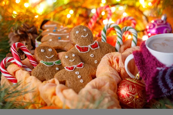 Biscuits in the form of little men for Christmas and hot drink cocoa on a background of a garland and a box in the form of a Christmas tree. Christmas tale. — Stock Photo, Image