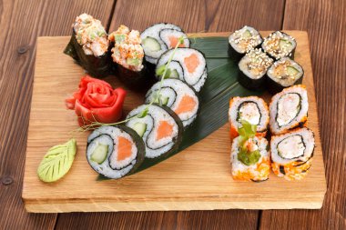 Suşi adet farklı türde tutan bir ahşap plaka. suşi ve ahşap plaka üzerinde rulo zencefil ve wasabi ile hizmet.