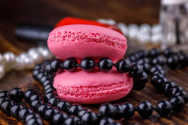 Makronen von Keksen in rosa Farbtönen auf einem hölzernen Hintergrund mit Make-up-Produkten. — Stockfoto