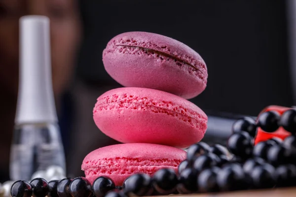 Pirámide de macarrones de tonos rosados sobre un fondo de madera con un tubo de barniz para la manicura perfecta . — Foto de Stock