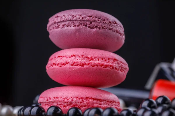 Macaroons of pink shades on a wooden background with a tube of lacquer for perfect manicure and a thread of beads. — Stock Photo, Image